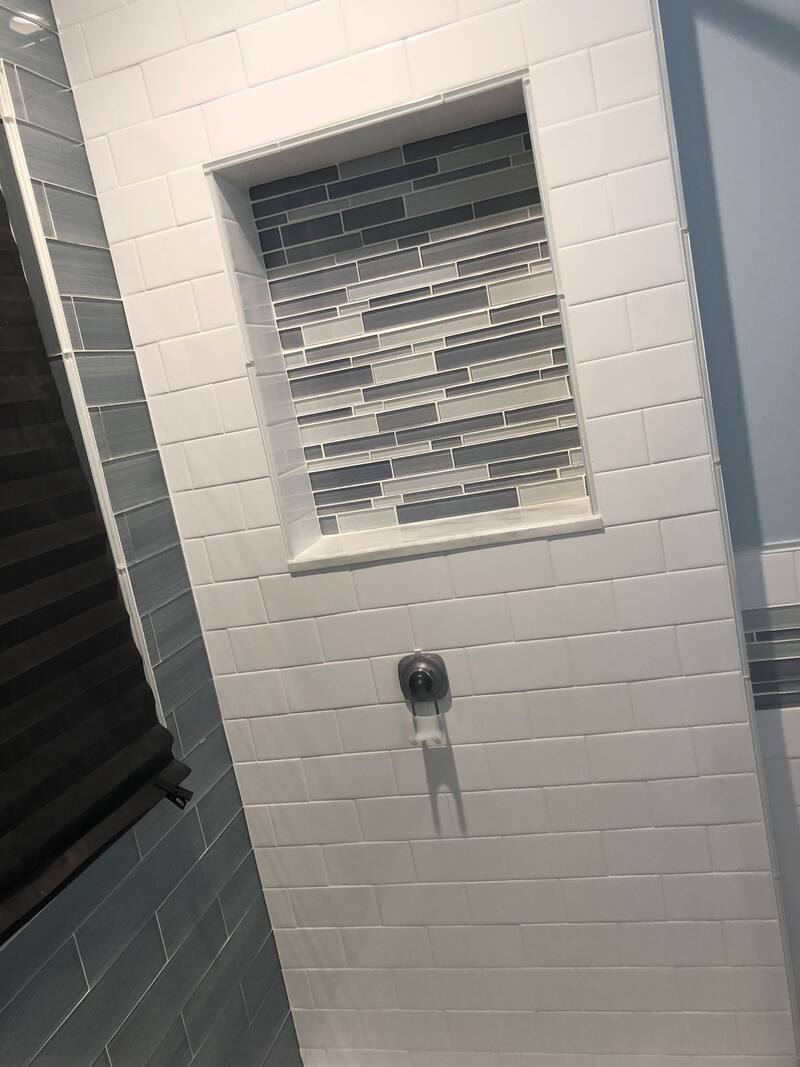 Close-up of a tiled shower wall with a mosaic accent strip