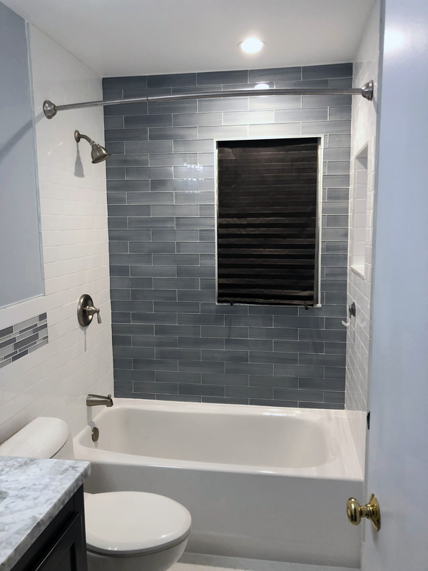 Bathtub surround in white tile with a grey glass mosaic band